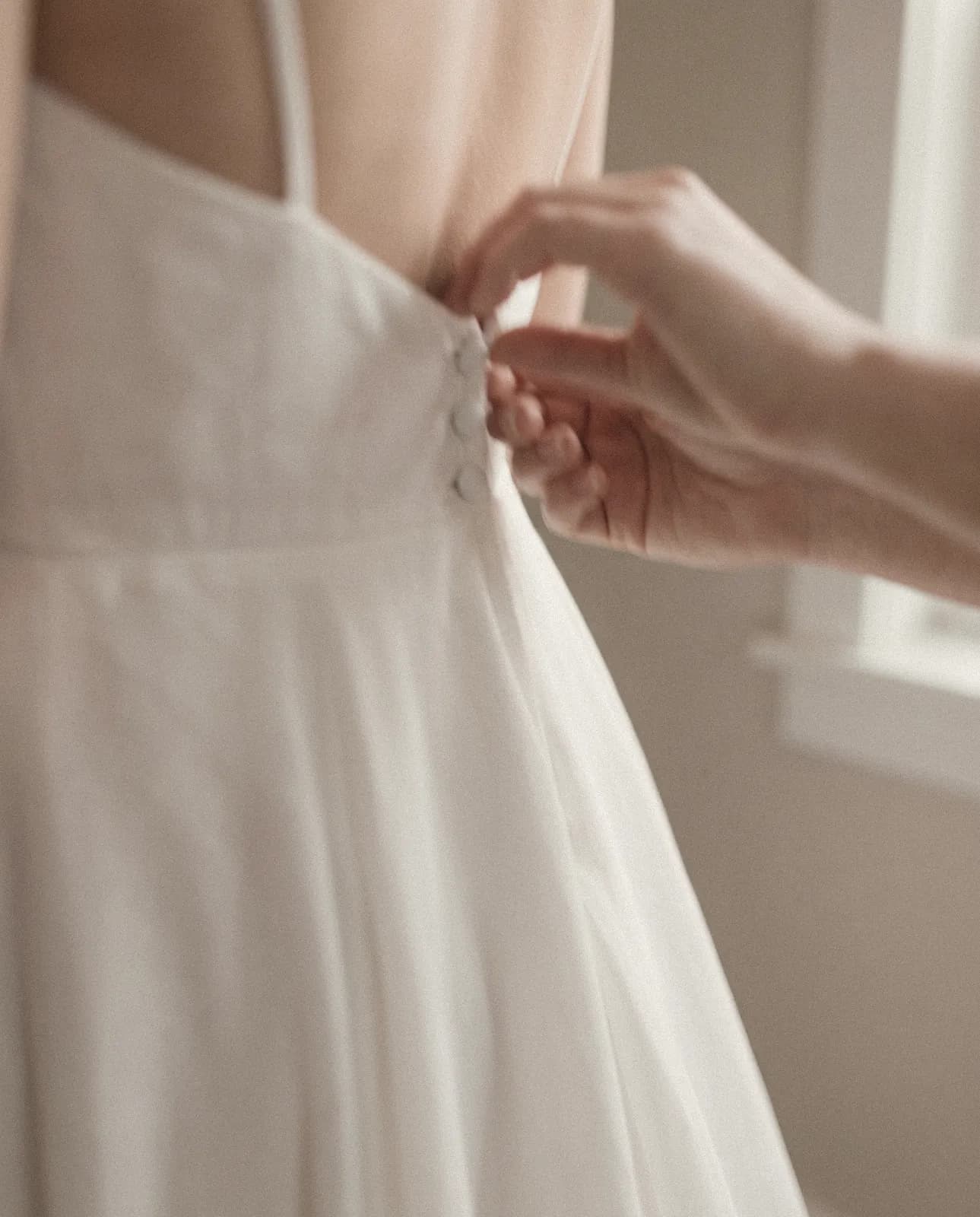 Unas manos abrochan los botones en la espalda de un vestido de novia